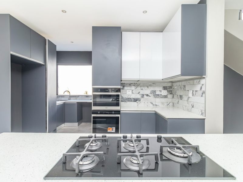 Modern kitchen featuring sleek grey and white cabinetry, stone countertops, a built-in oven, microwave, and a gas hob on the central island.