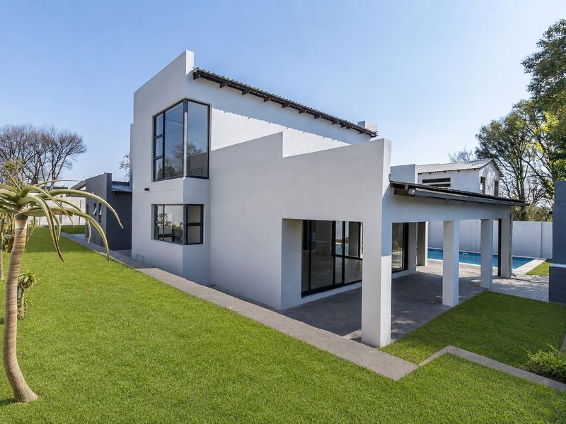 Modern rear elevation featuring a covered patio, paved terrace, and swimming pool set within a well-maintained landscaped garden.