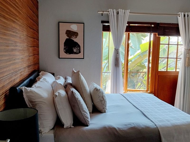 A well-maintained bedroom featuring a decorative wood-paneled accent wall, a ceiling fan, and direct access to an outdoor area through a timber-framed door.