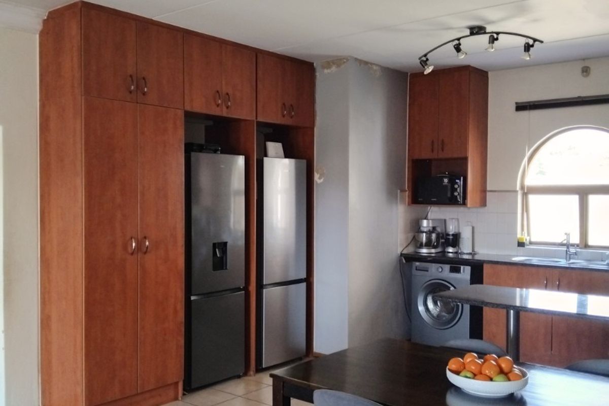 Kitchen area featuring wooden cabinetry, tiled flooring, and an arched window, with integrated appliance spaces and a functional layout.