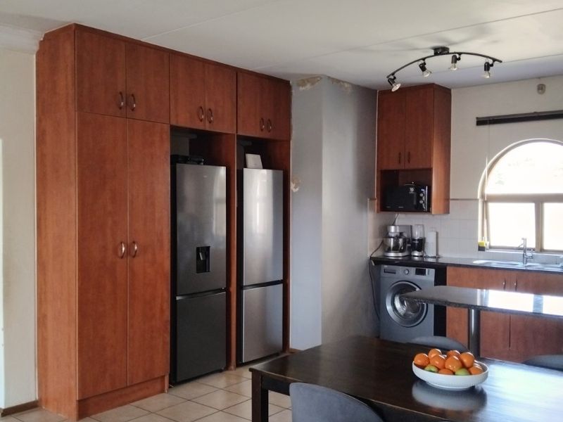 Kitchen area featuring wooden cabinetry, tiled flooring, and an arched window, with integrated appliance spaces and a functional layout.