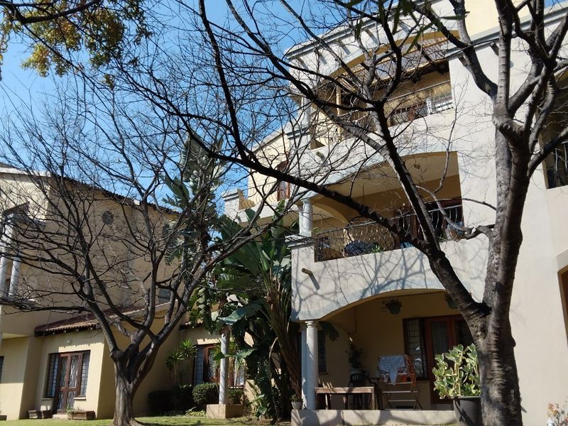 Rear view of a multi-story apartment building featuring covered balconies, ground floor patios, and established garden landscaping.