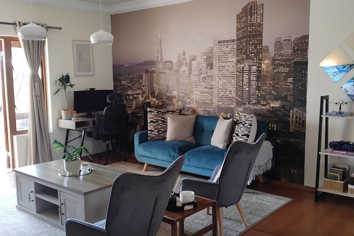 A well-maintained living room featuring laminate flooring, decorative ceiling cornices, and pendant lighting, with access to an outdoor area via a sliding door.