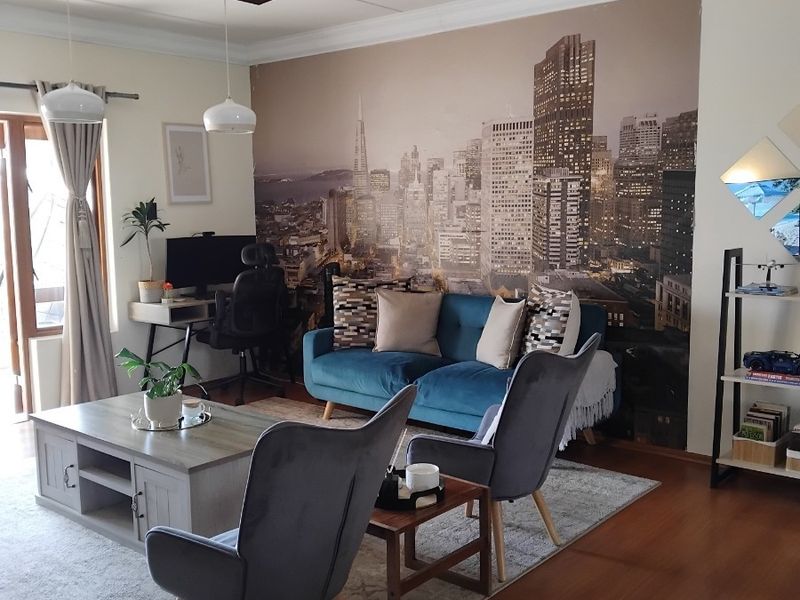 A well-maintained living room featuring laminate flooring, decorative ceiling cornices, and pendant lighting, with access to an outdoor area via a sliding door.
