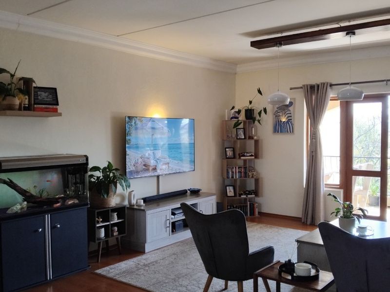 A comfortable living room featuring a mix of laminate and tiled flooring, decorative ceiling beams, and direct access to an outdoor balcony area.