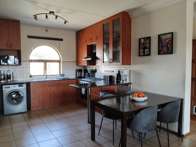 Open-plan kitchen featuring wooden cabinetry, granite countertops, built-in appliances, and tiled flooring, seamlessly integrated with a dining area.