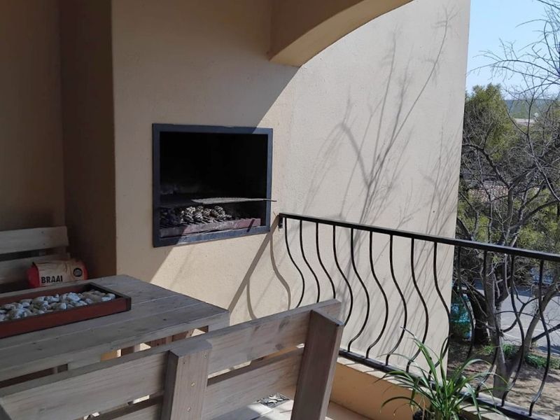Covered balcony featuring a built-in braai, tiled flooring, and a decorative wrought iron balustrade overlooking the surrounding area.