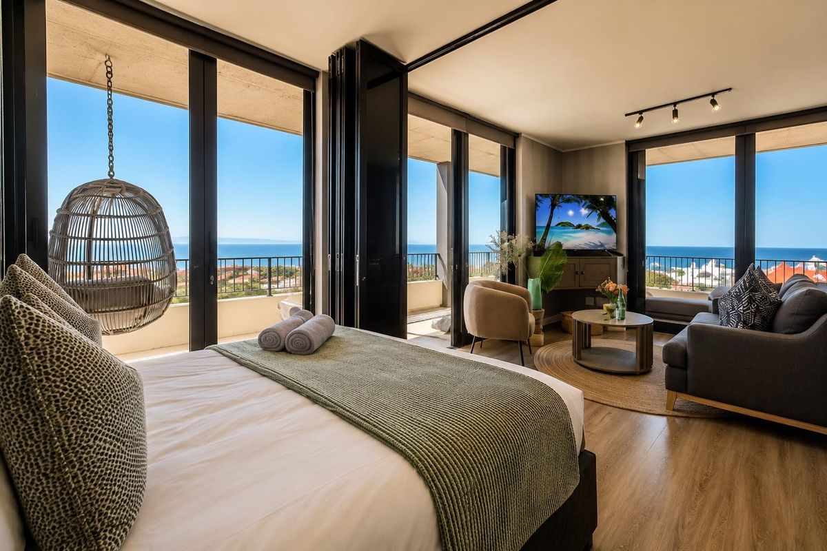 Spacious bedroom featuring large bi-fold doors opening onto a private balcony with expansive ocean views and modern laminate flooring.