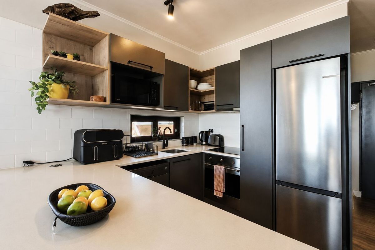 Modern kitchen featuring dark cabinetry, quartz countertops, subway tile backsplash, integrated appliances, and stylish track lighting in a well-maintained apartment setting.