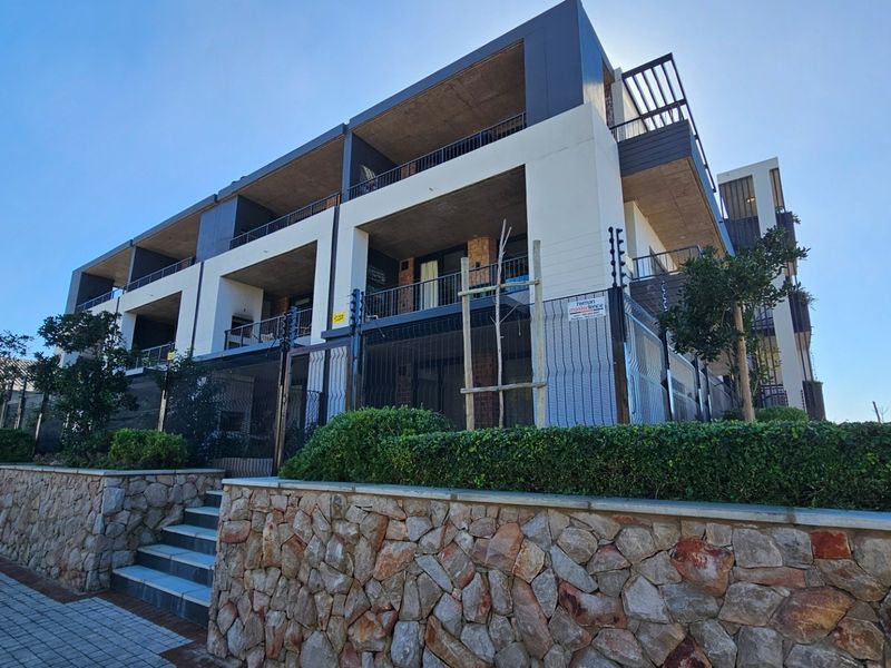Modern apartment complex exterior featuring stone retaining walls, secure electric fencing, and private balconies with contemporary architectural design.