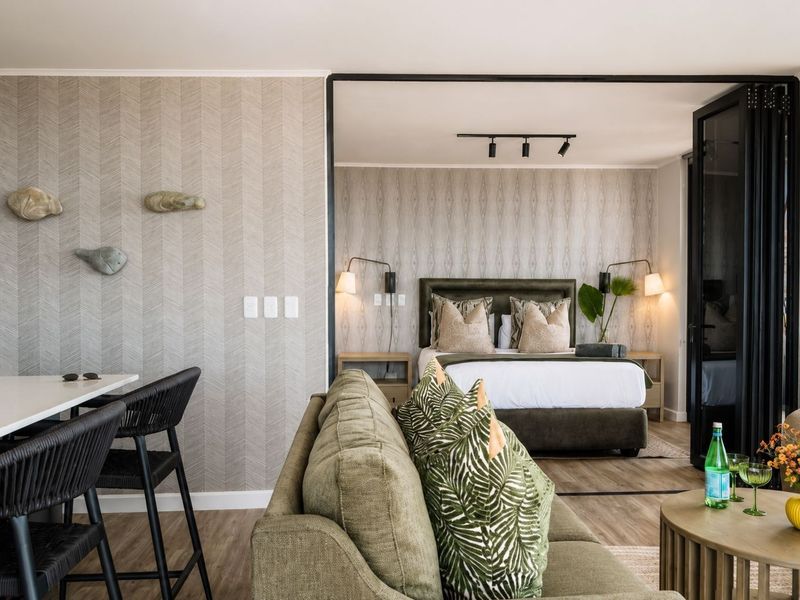 A modern open-plan apartment interior featuring a bedroom separated by black-framed bi-fold glass doors, complemented by stylish textured wallpaper and contemporary lighting fixtures.