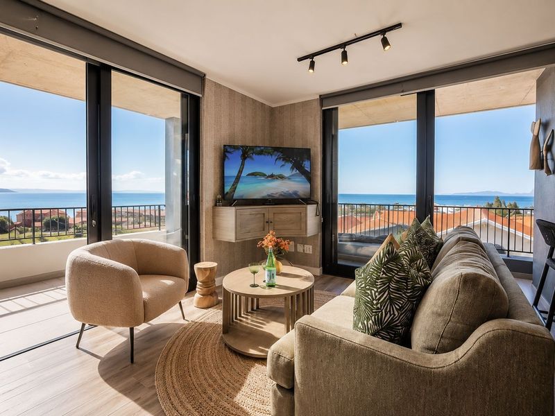 Modern living room featuring large sliding glass doors with panoramic ocean views, tiled flooring, and contemporary track lighting.