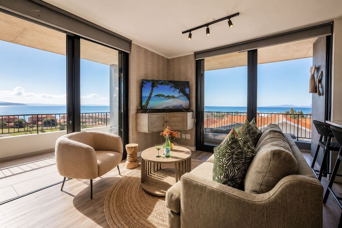 Modern living room featuring large sliding glass doors with panoramic ocean views, tiled flooring, and contemporary track lighting.