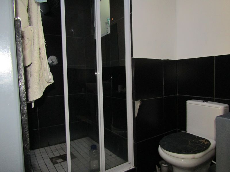A compact bathroom featuring a shower enclosure and toilet with black wall tiling. The space shows signs of wear and requires maintenance.