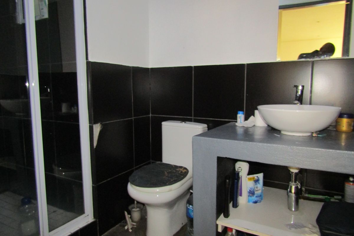 A compact bathroom featuring a shower enclosure, a modern vessel sink on a concrete vanity base, and dark wall tiling.