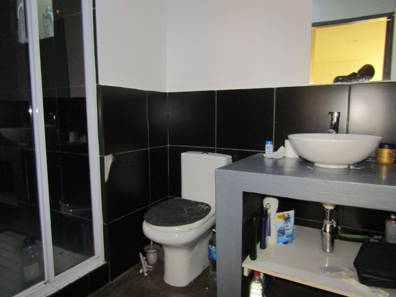 A compact bathroom featuring a shower enclosure, a modern vessel sink on a concrete vanity base, and dark wall tiling.