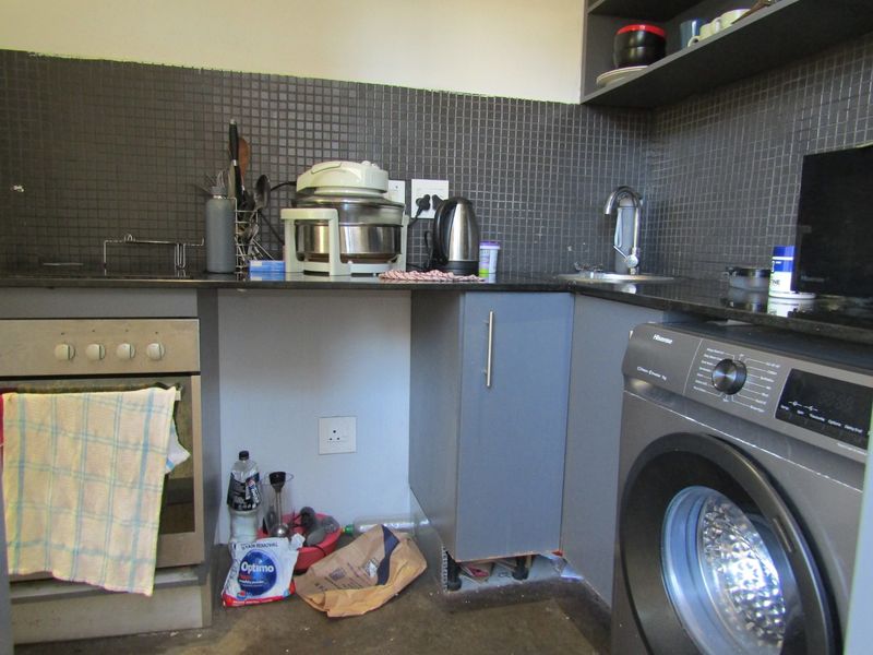 Compact kitchen featuring dark mosaic tile backsplash, granite countertops, built-in oven, and integrated laundry space with open shelving.
