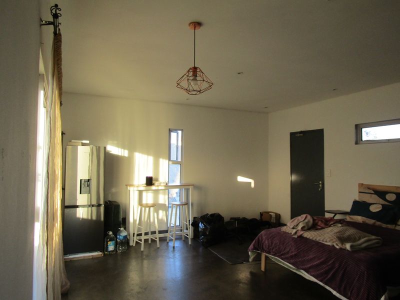 A bedroom featuring polished concrete flooring, modern pendant lighting, and dual-aspect windows providing natural light.