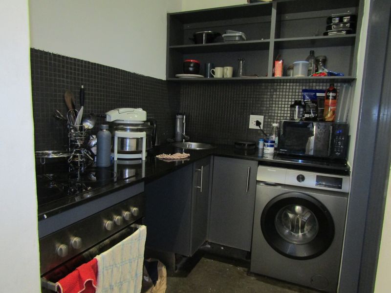 Compact kitchen featuring dark cabinetry, mosaic tile backsplash, granite countertops, built-in oven, and an integrated washing machine.