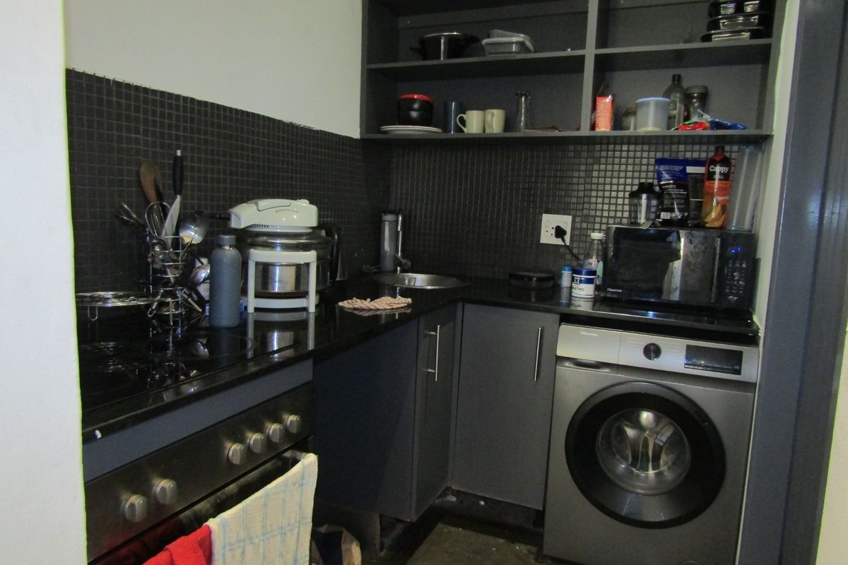 Compact kitchen featuring dark cabinetry, mosaic tile backsplash, granite countertops, built-in oven, and an integrated washing machine.