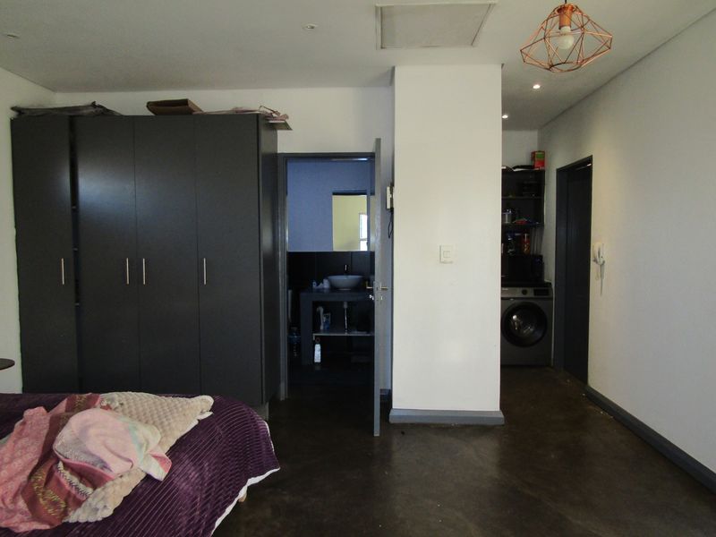 Bedroom featuring dark built-in wardrobes, polished concrete flooring, and direct access to an en-suite bathroom and laundry area.
