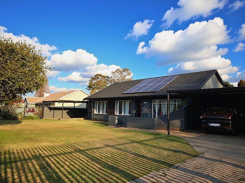 Front view of a well-maintained house featuring a tiled roof with solar panels, a paved driveway, and an attached carport.