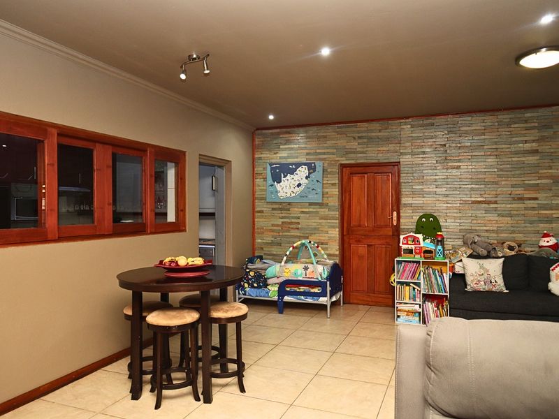 A living room featuring a stone veneer accent wall, tiled flooring, and timber door and window frames with integrated lighting.