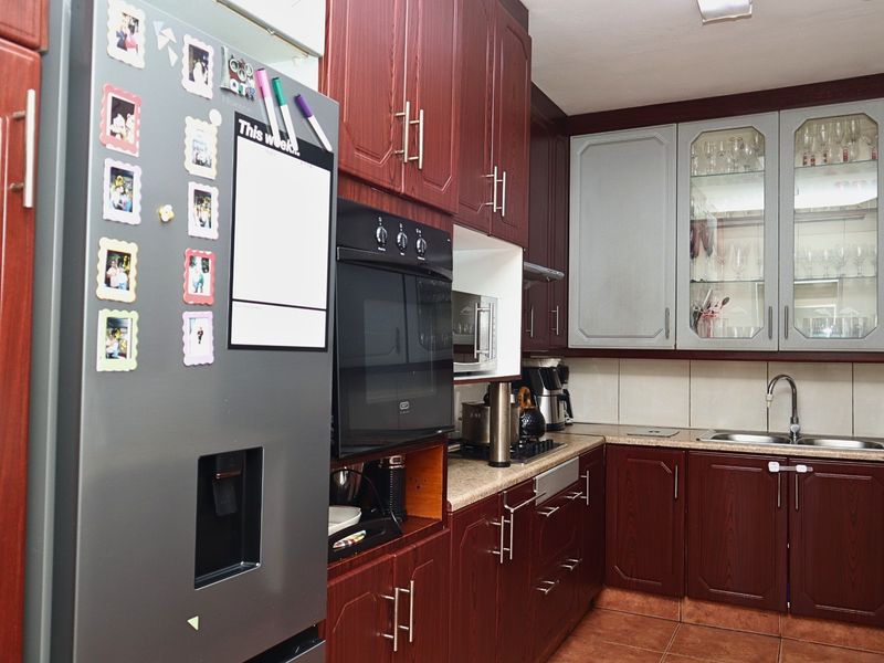 A functional kitchen featuring dark wood-finish cabinetry, built-in oven, hob, extractor fan, and a double sink with tiled backsplash.