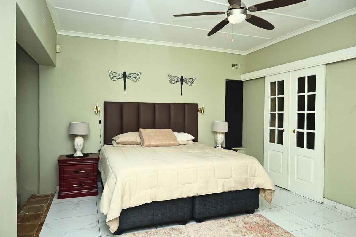 A well-lit bedroom featuring tiled flooring, a ceiling fan, and sliding glass doors providing access to the exterior.