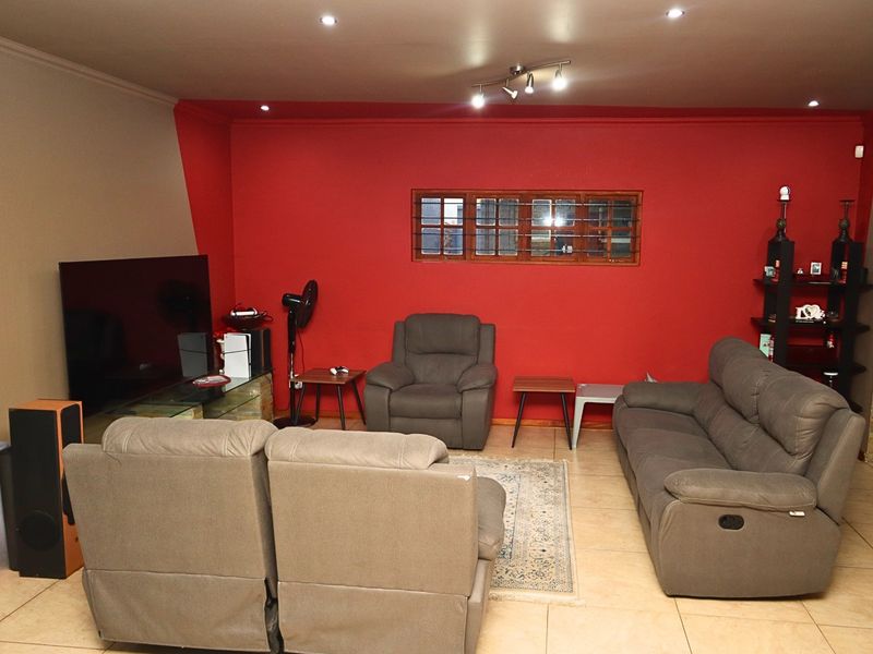 A spacious living room featuring tiled flooring, recessed downlighting, and a bold red accent wall with an internal window feature.