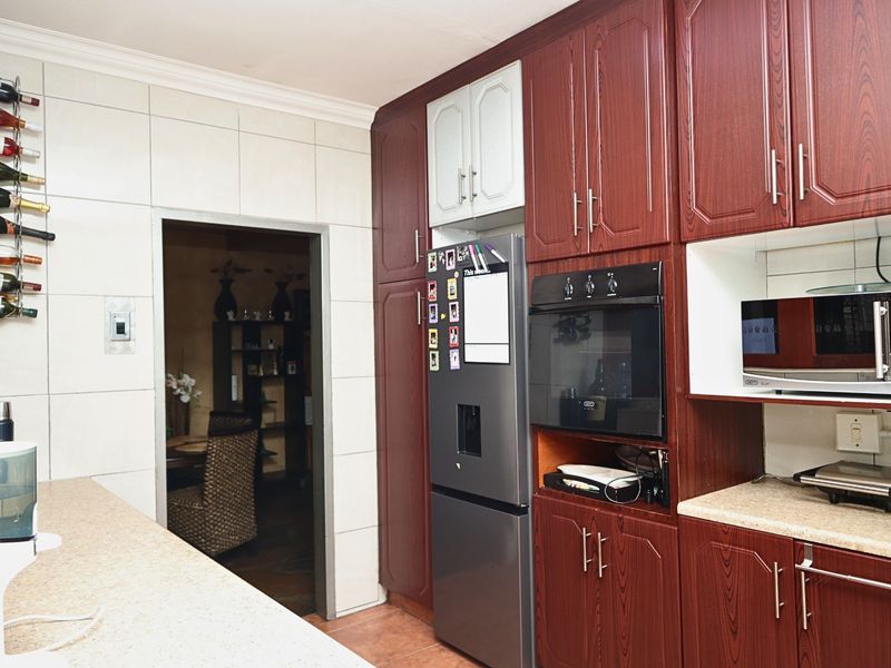 A functional kitchen featuring dark wood-grain cabinetry, laminate countertops, and integrated appliance housing, providing a practical layout with tiled wall finishes.