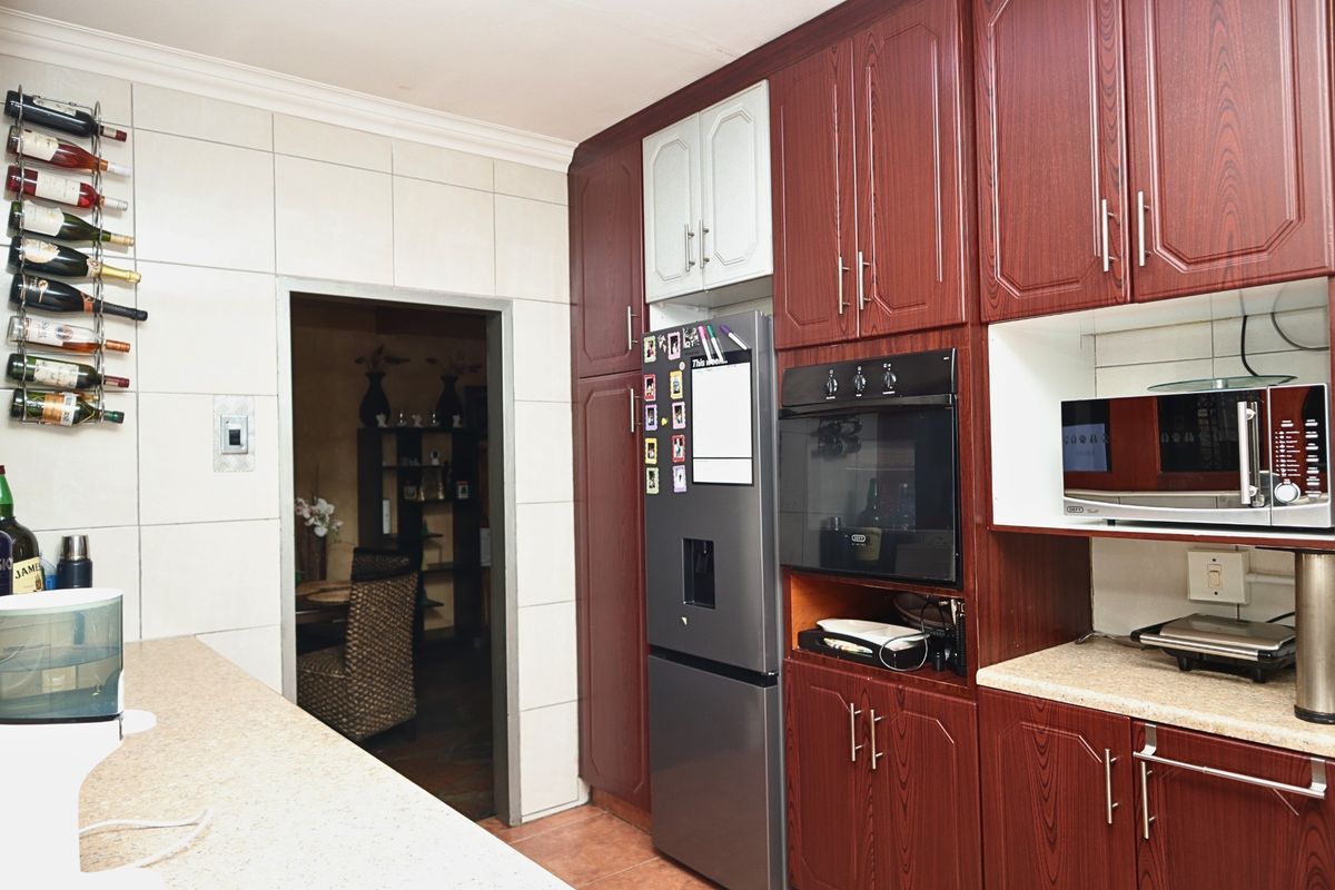 A functional kitchen featuring dark wood-grain cabinetry, laminate countertops, and integrated appliance housing, providing a practical layout with tiled wall finishes.