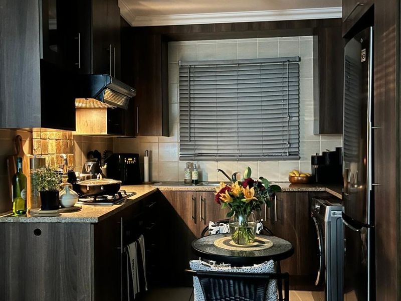 A compact, well-maintained kitchen featuring dark wood cabinetry, stone countertops, tiled backsplash, and integrated appliances, offering a functional and modern cooking space.