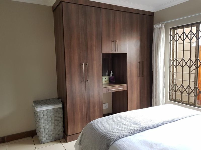 Bedroom featuring a large dark wood built-in wardrobe with an integrated vanity station and a window fitted with a security gate.