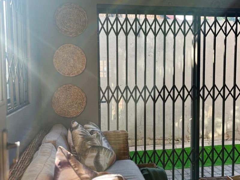 A living area featuring tiled flooring, a sliding door with a security gate, and security bars on the window, opening to an outdoor space.