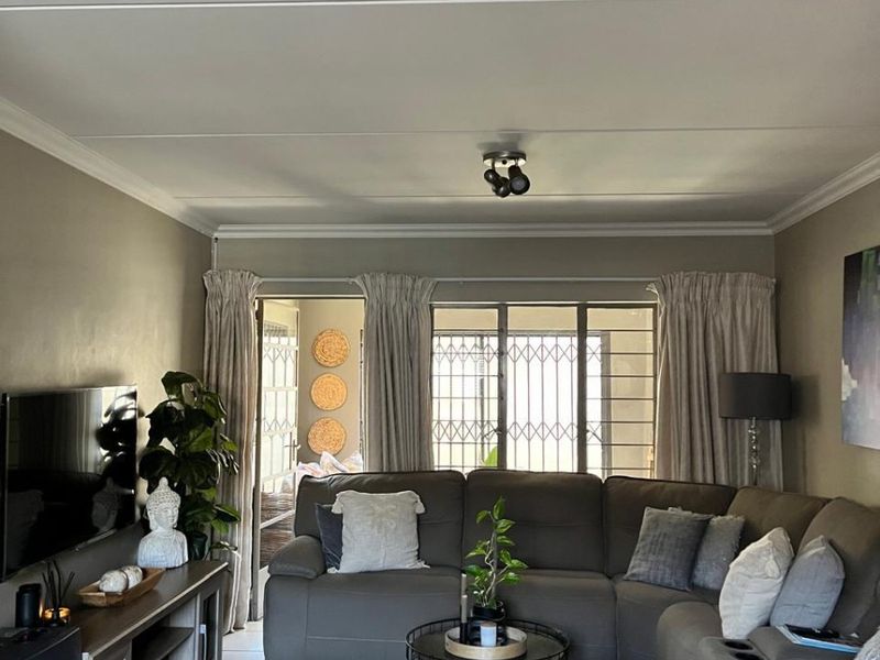 A comfortable living room featuring tiled flooring, ceiling cornicing, and a sliding door leading to an outdoor area with security gate access.
