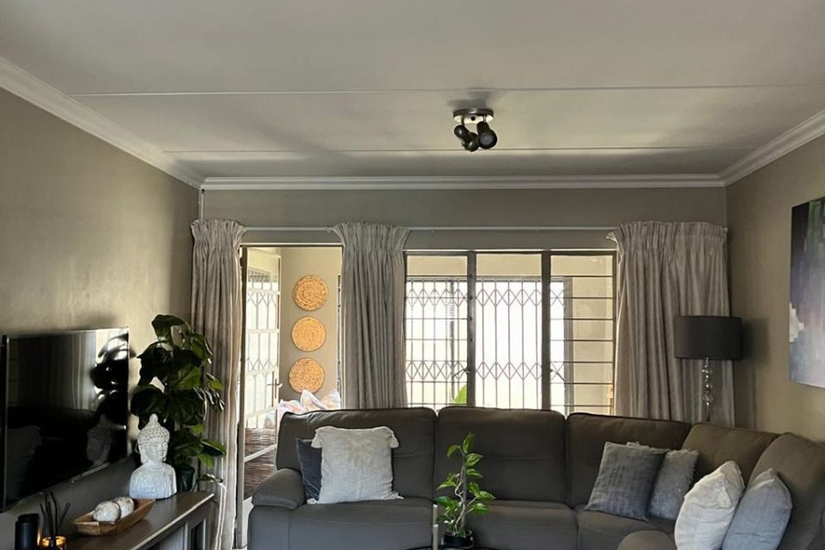 A comfortable living room featuring tiled flooring, ceiling cornicing, and a sliding door leading to an outdoor area with security gate access.