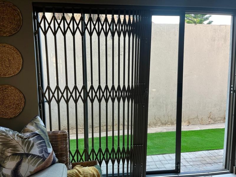 Living area featuring a sliding glass door with a retractable security gate, opening onto a small paved patio and artificial lawn area.