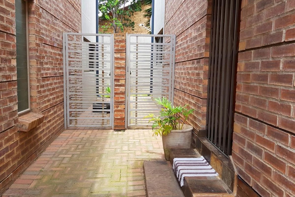 A private rear courtyard featuring exposed brick walls, paved flooring, and a secure metal gate entrance.