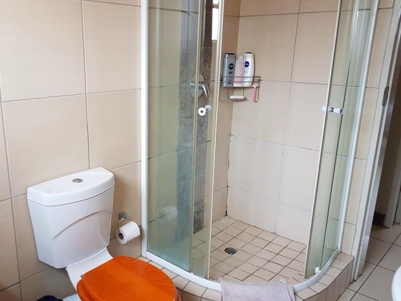 A functional bathroom featuring a corner shower enclosure with tiled walls and a standard toilet.