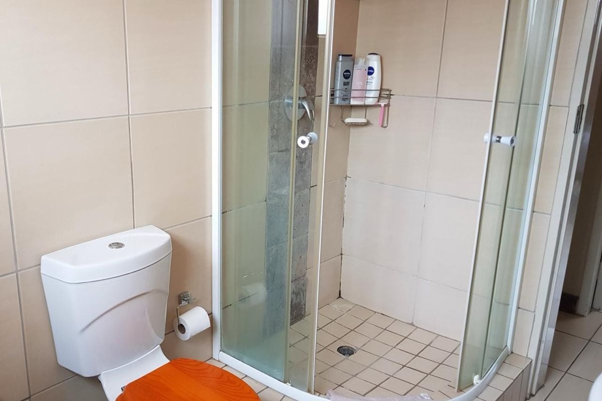 A functional bathroom featuring a corner shower enclosure with tiled walls and a standard toilet.