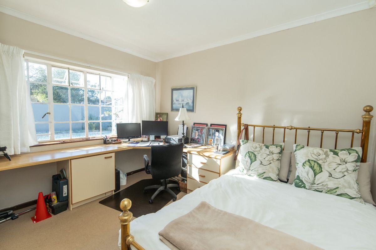 A bedroom featuring a built-in corner desk workspace, large multi-pane window, and neutral wall finishes.