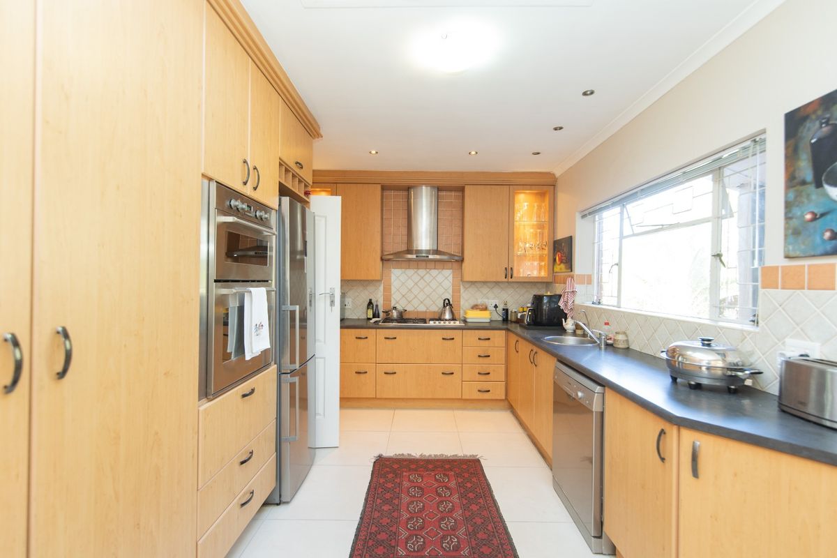 A functional kitchen featuring light wood cabinetry, a stainless steel oven and extractor fan, tiled backsplash, and dark countertops.