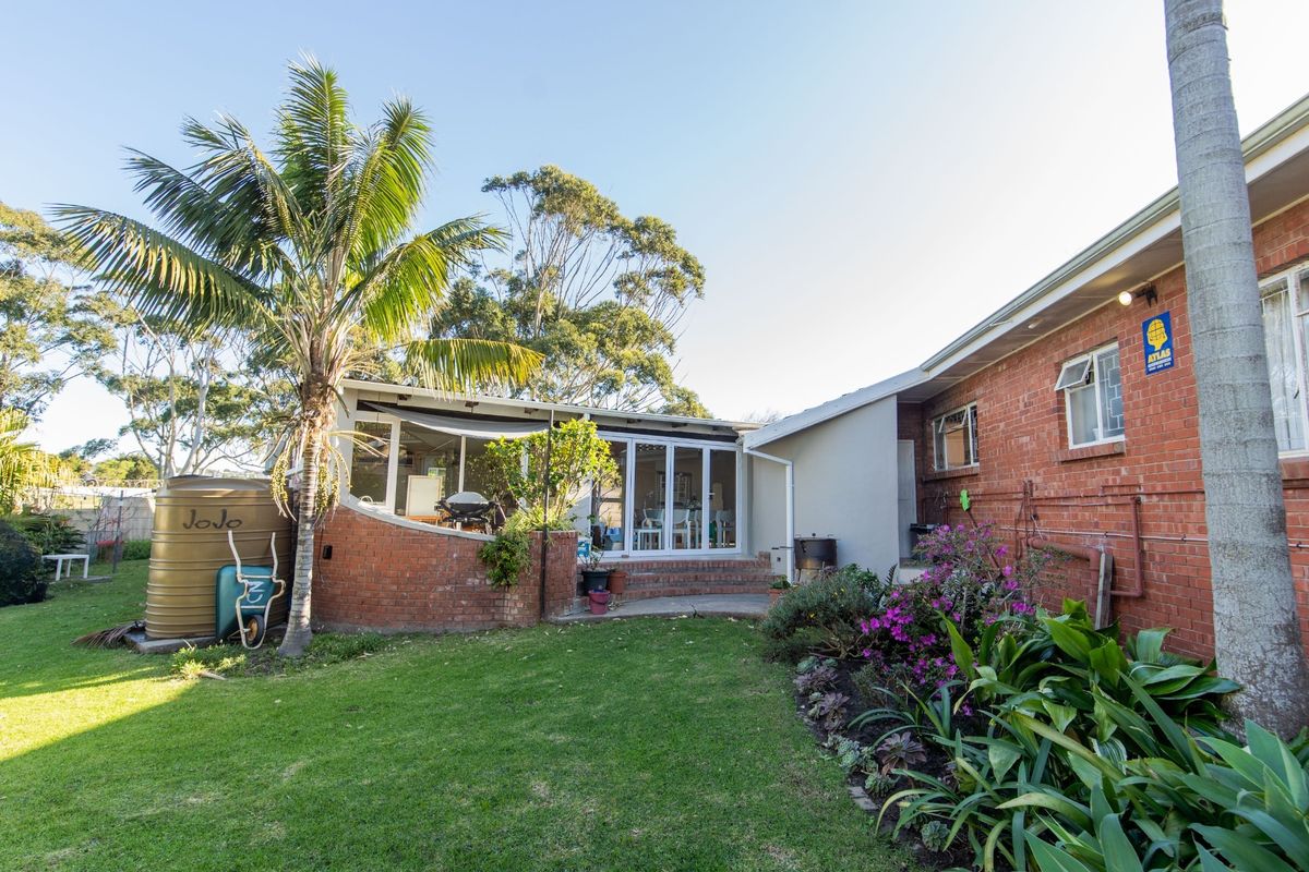 Rear view of the property featuring a brick facade, a paved patio area with sliding glass doors, and a well-maintained garden with a water tank.