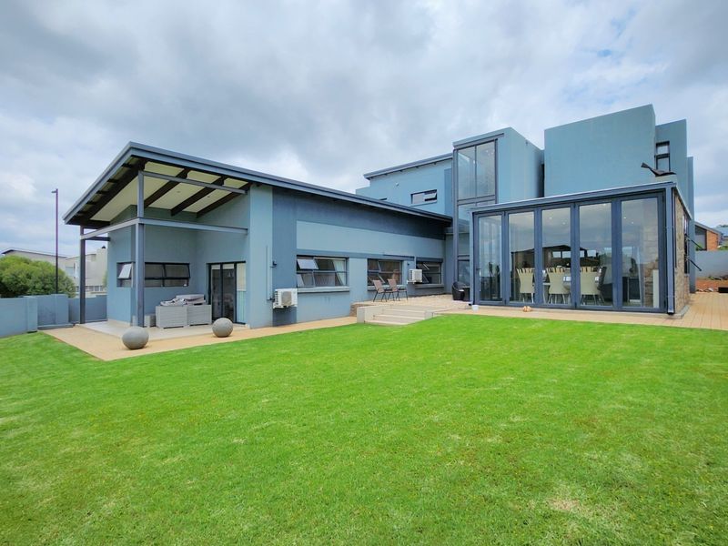 Rear view of a modern multi-level home featuring a spacious lawn, covered patio area, and large glass bi-fold doors leading into the living space.