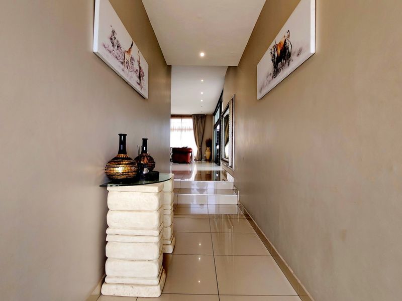 A well-lit hallway featuring polished floor tiles and a stepped transition leading into the main living area.