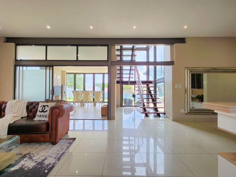 Spacious open-plan living area featuring polished porcelain tiles, a modern steel staircase, and large sliding glass doors leading to an outdoor dining space.