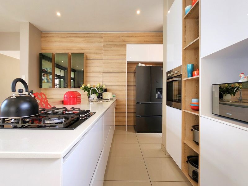 Modern kitchen featuring sleek white cabinetry, wood-look paneling, stone countertops, a gas hob, and integrated appliances with recessed lighting.