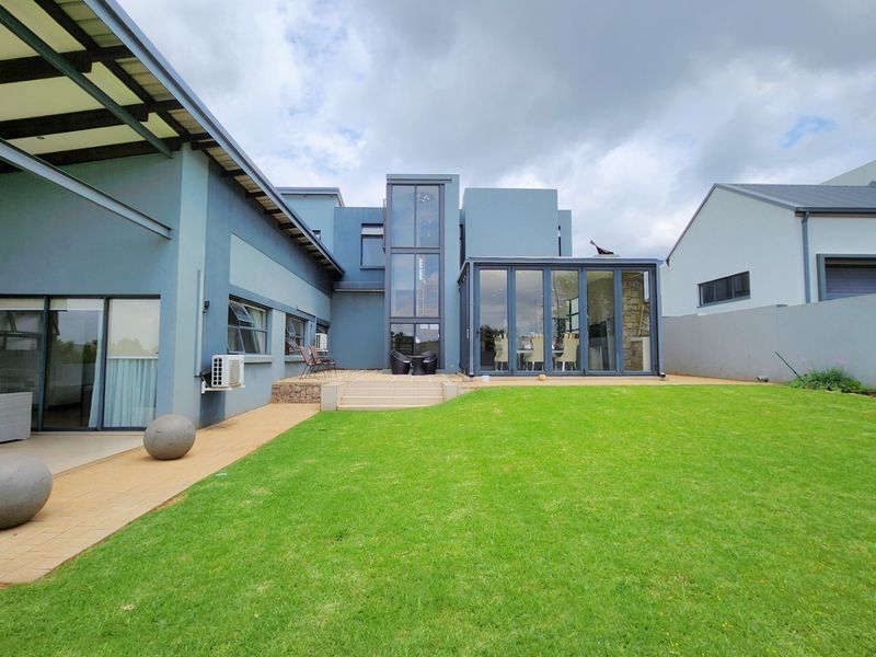 Rear view of a modern house featuring a spacious lawn, paved patio area, and large glass sliding doors leading into the living space.