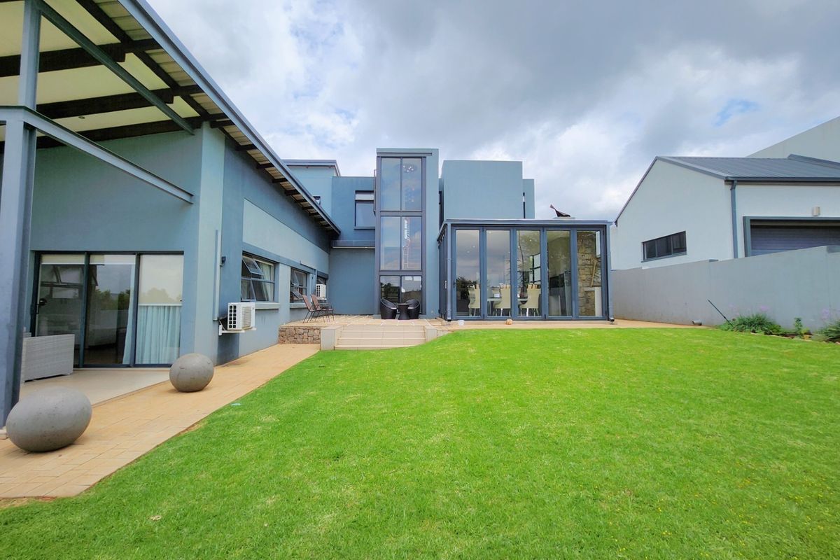 Rear view of a modern house featuring a spacious lawn, paved patio area, and large glass sliding doors leading into the living space.